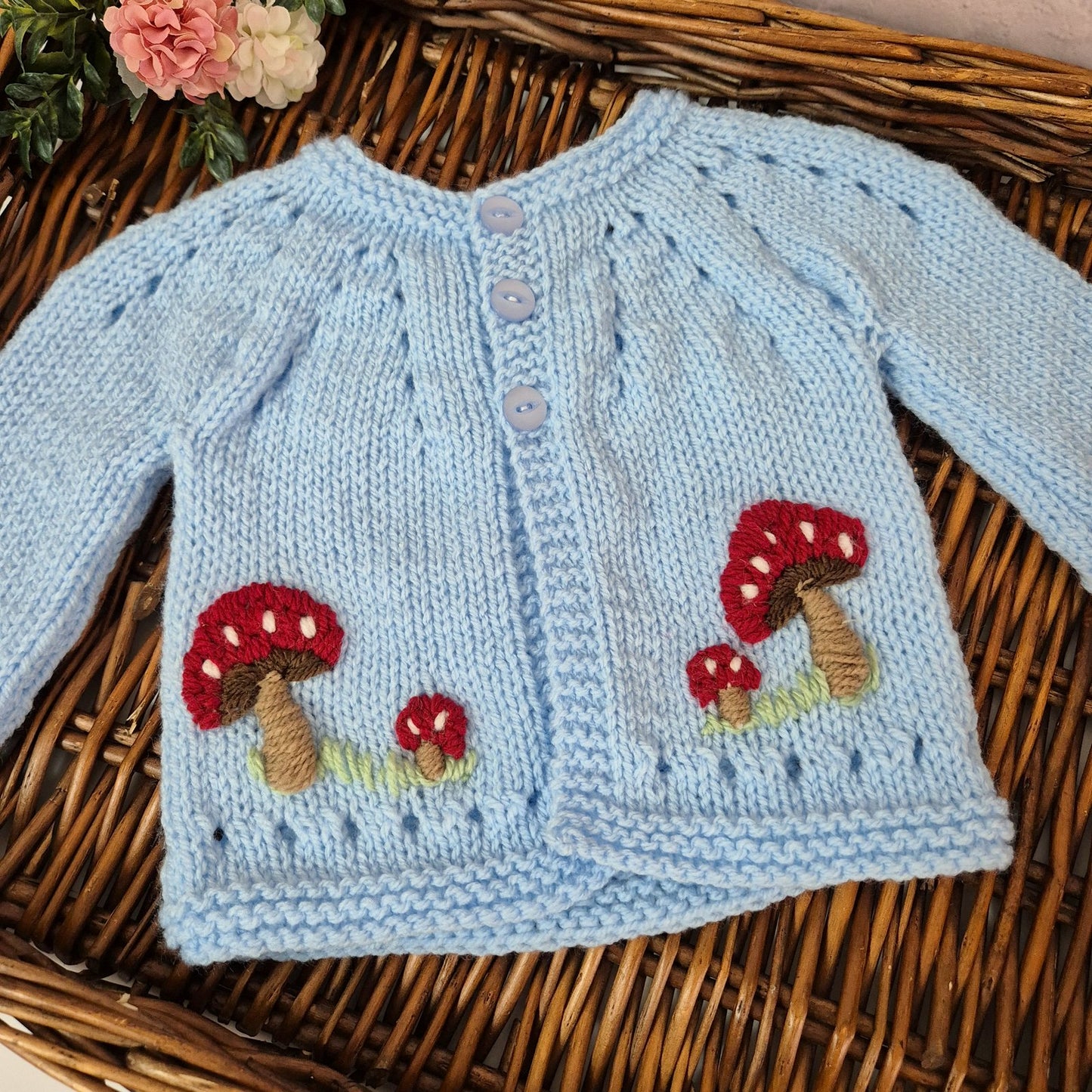 Light blue knitted cardigan with mushroom designs on a wicker surface.