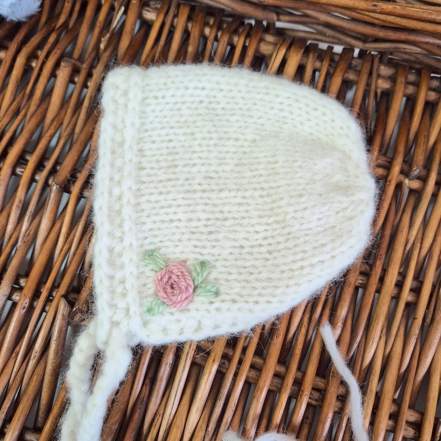 Knitted baby hat with a pink rose design on a wicker surface
