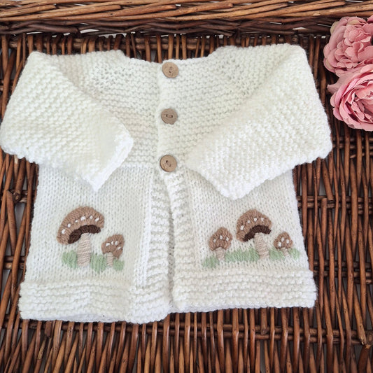 Knitted baby cardigan with mushroom patterns on a wicker surface