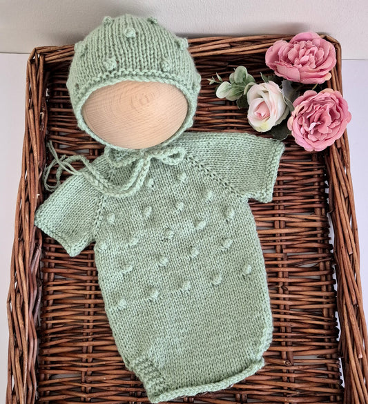 Knitted green baby outfit with bonnet on a woven tray with flowers