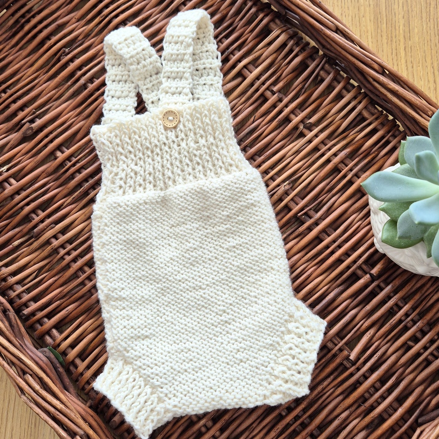 Ready to send knitted baby romper with shoulder straps, suitable for newborn photography.
Knit in cream merino yarn, this little dungaree type romper has a wide ribbed chest, and garter stitching on the tummy/ diaper.