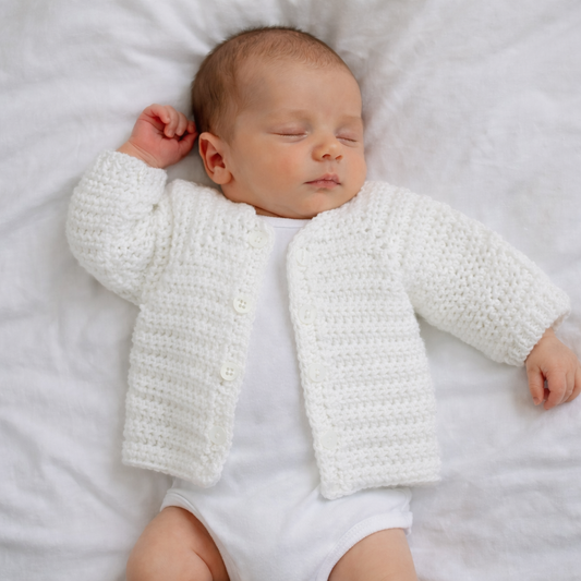 Newborn baby wearing a white crocheted cardigan on a white blanket