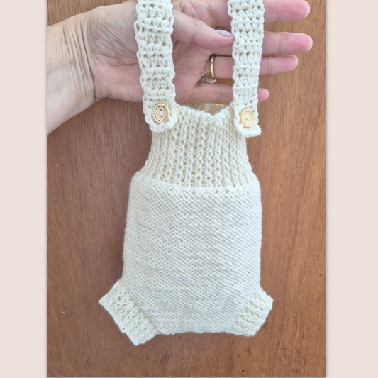 Ready to send knitted baby romper with shoulder straps, suitable for newborn photography.
Knit in cream merino yarn, this little dungaree type romper has a wide ribbed chest, and garter stitching on the tummy/ diaper.