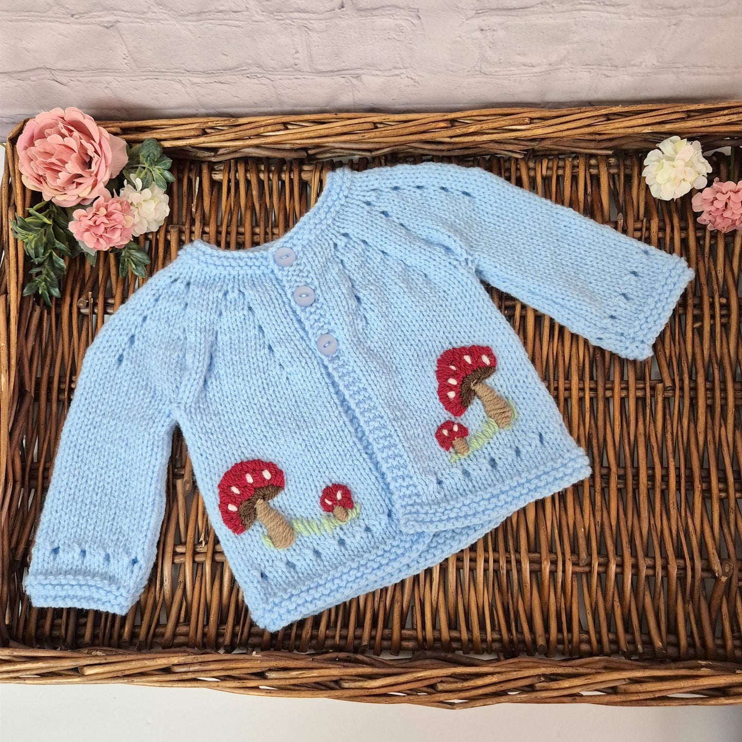 Knitted baby sweater with mushroom design on a woven surface with flowers.