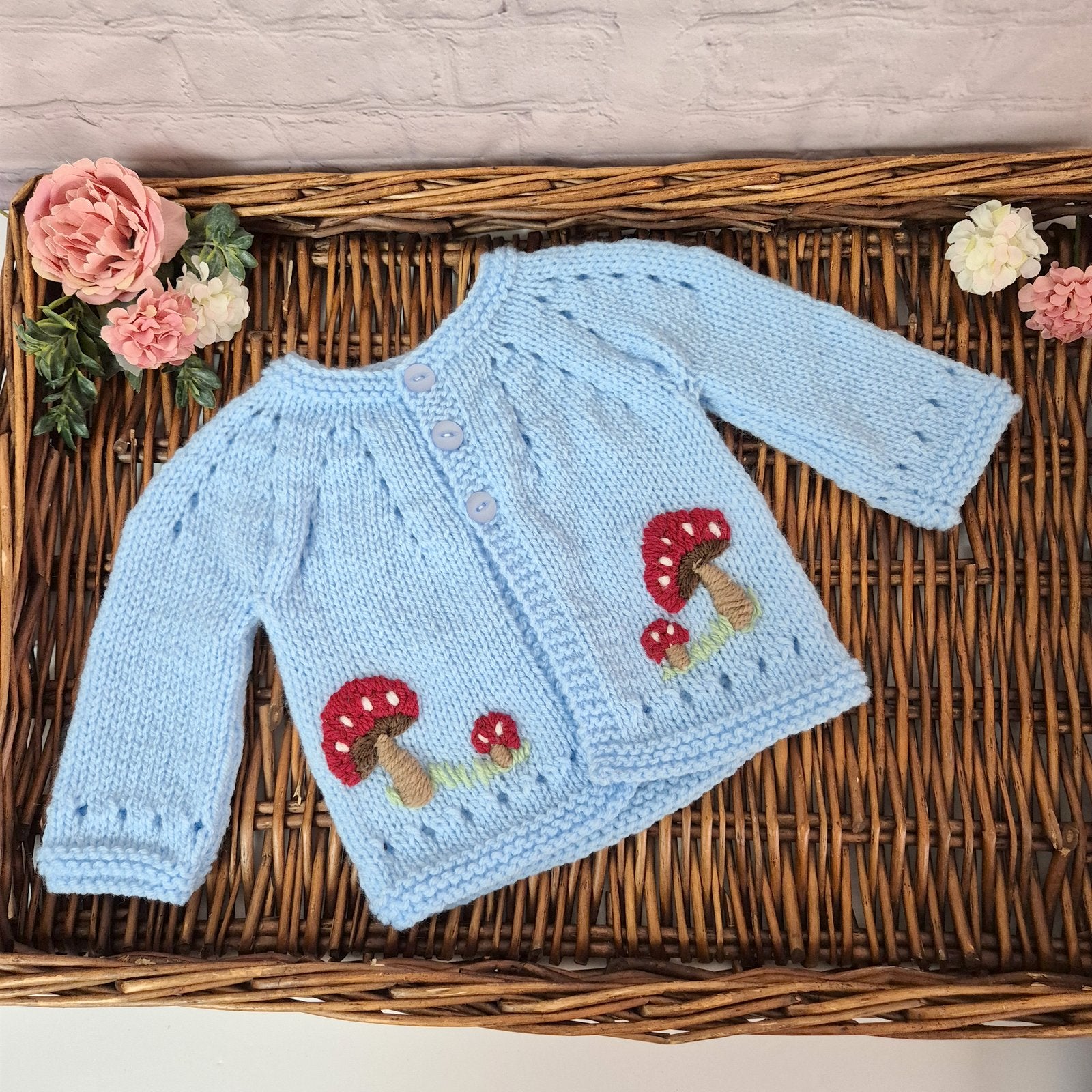 Knitted baby sweater with mushroom design on a woven surface with flowers.