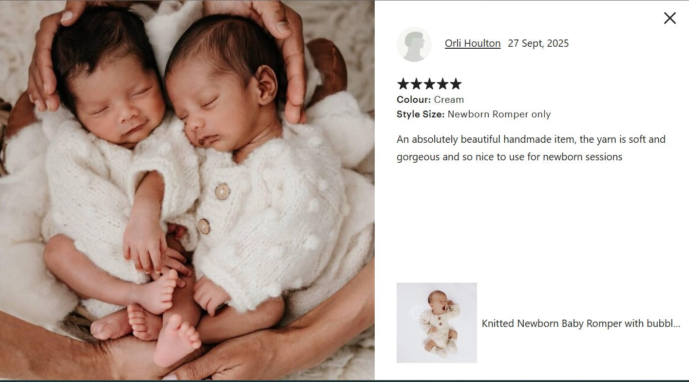 Two newborn babies in white knitted rompers being held by an adult.