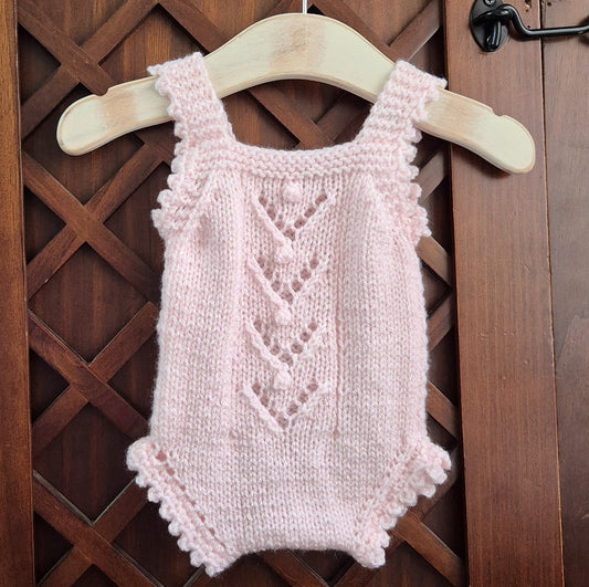 Pink knitted baby romper on a wooden hanger against a wooden lattice background. RTS Newborn Pink Lacy Popcorn knitted baby girl romper. (Ready to send)