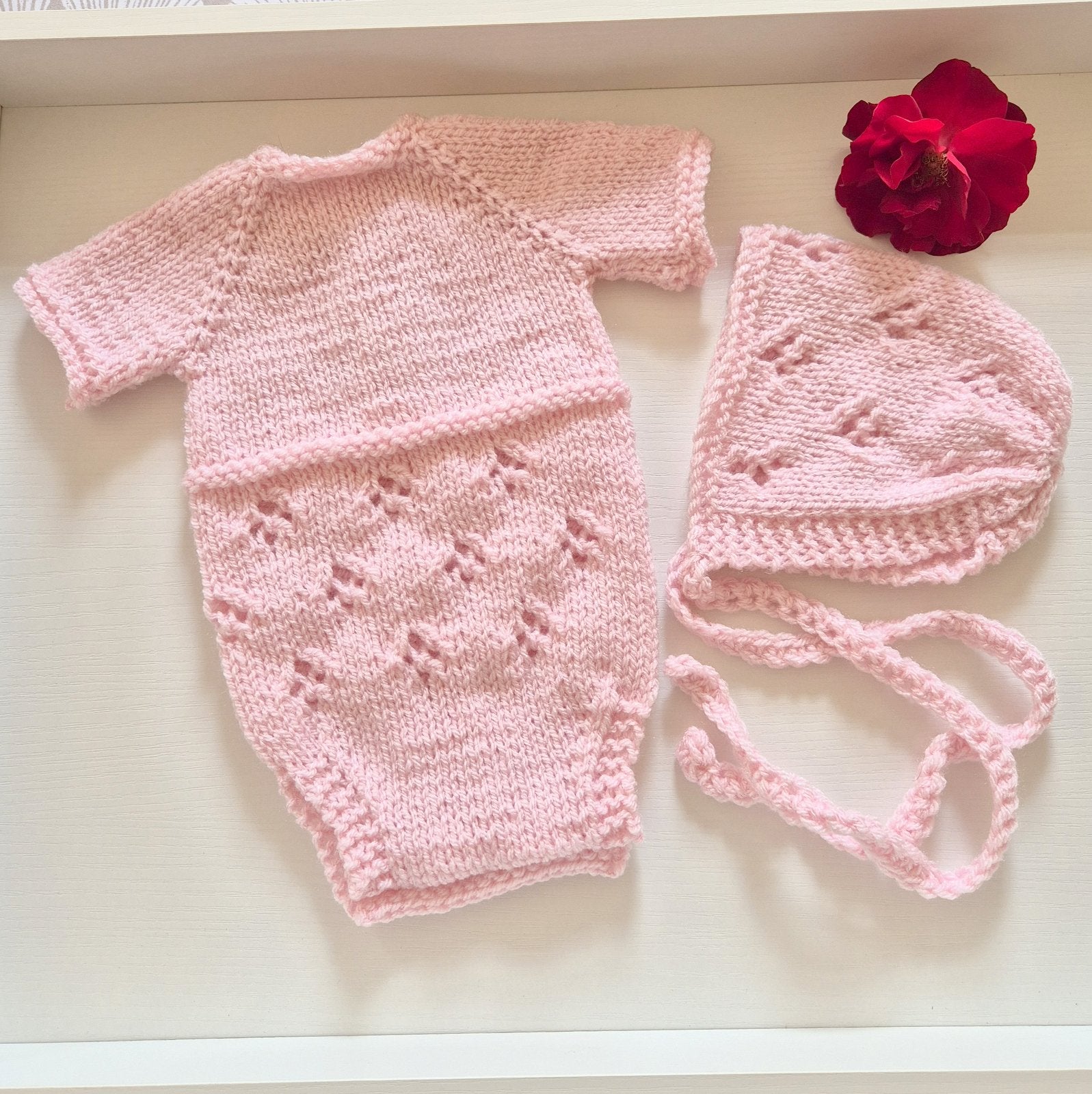 Pink Handknit Newborn Baby Romper and Bonnet Set. Knit in soft quality acrylic yarn, in an eyelet lace pattern. This short sleeved bodysuit style romper is suitable as a hospital coming home outfit, newborn photo prop or baby shower gift. Ready to send.
The little romper has buttons at the neck that can be worn to the back or the front,&nbsp; and for buttons for quick diaper changes.
Shipped from the UK, in an organza bag that is ready for you to gift.