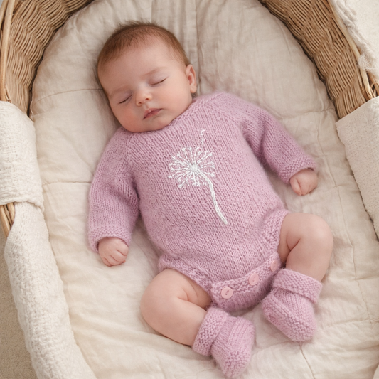 Newborn baby in a pink knitted outfit lying in a basket. pink knitted onesie with matching booties and embroidered with a dandelion