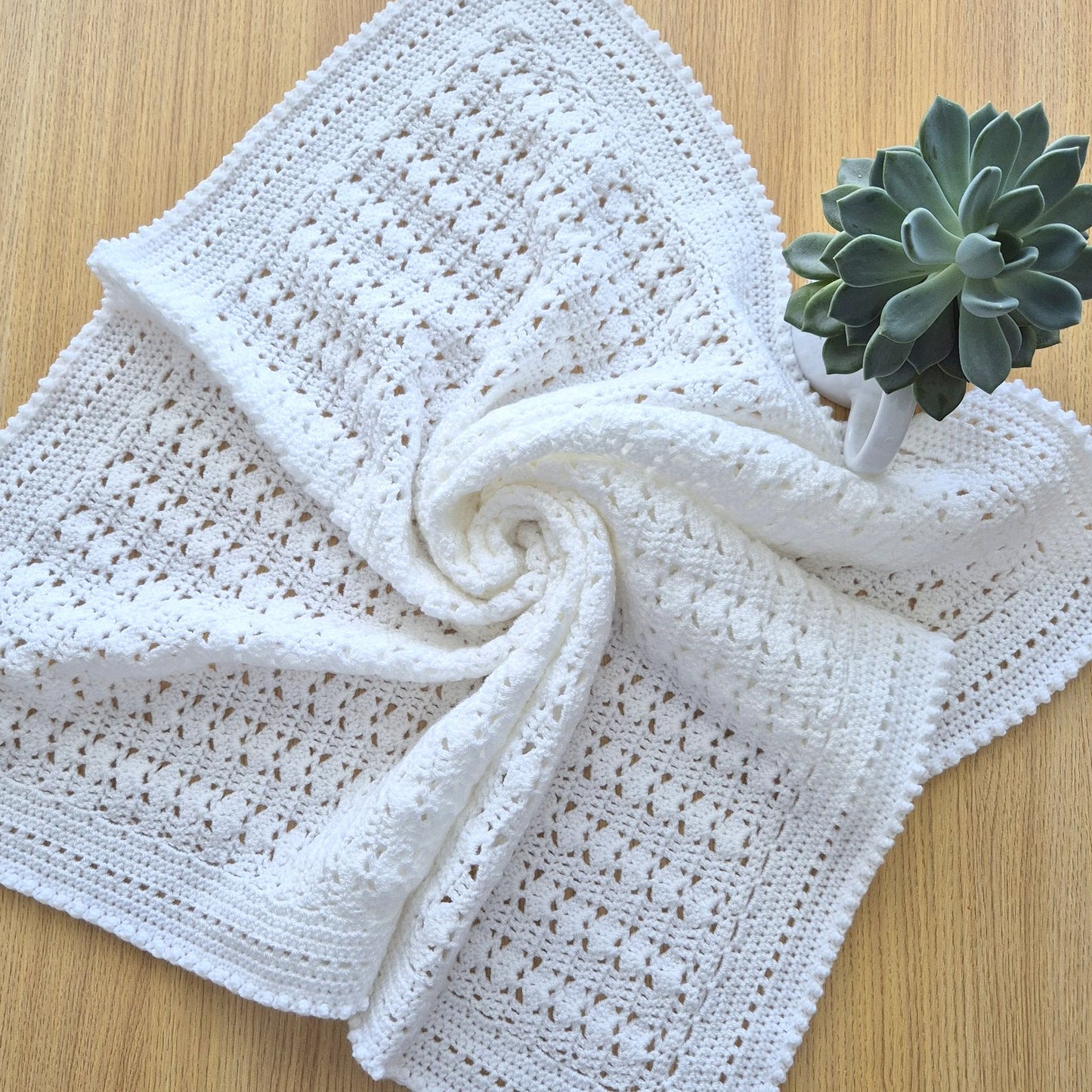White crocheted blanket on a wooden surface with a small plant.