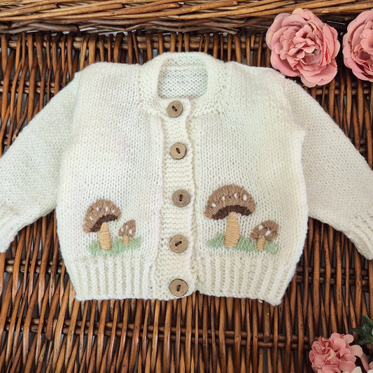 White hand knit baby cardigan with embroidered brown button mushrooms. Jumper, 0-3 months Sweater. with a little pixie dust sparkle to the yarn.
A gorgeous hand knit baby cardigan to fit a baby of 0-3 months This little jumper has coconut shell buttons with adorable embroidery on the front.