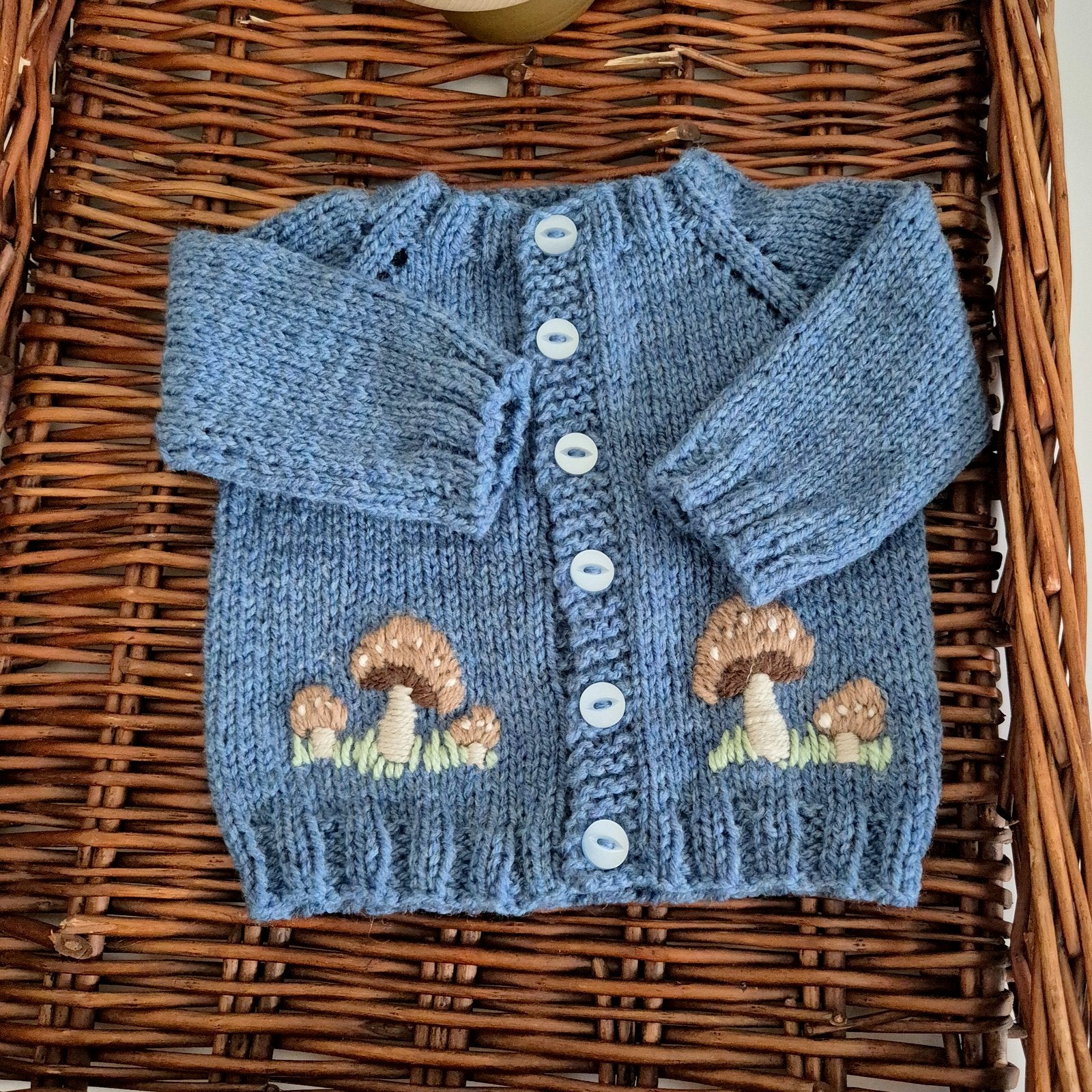 Knitted Dark Blue cardigan and hat set for a baby boy.  The set comprises a gorgeous hand knit baby cardigan with brown embroidered toadstool mushrooms on the front. A matching beanie completes the set. 
Designed to fit a 0-3 month old baby. The cardigan has blue buttons down the front. 