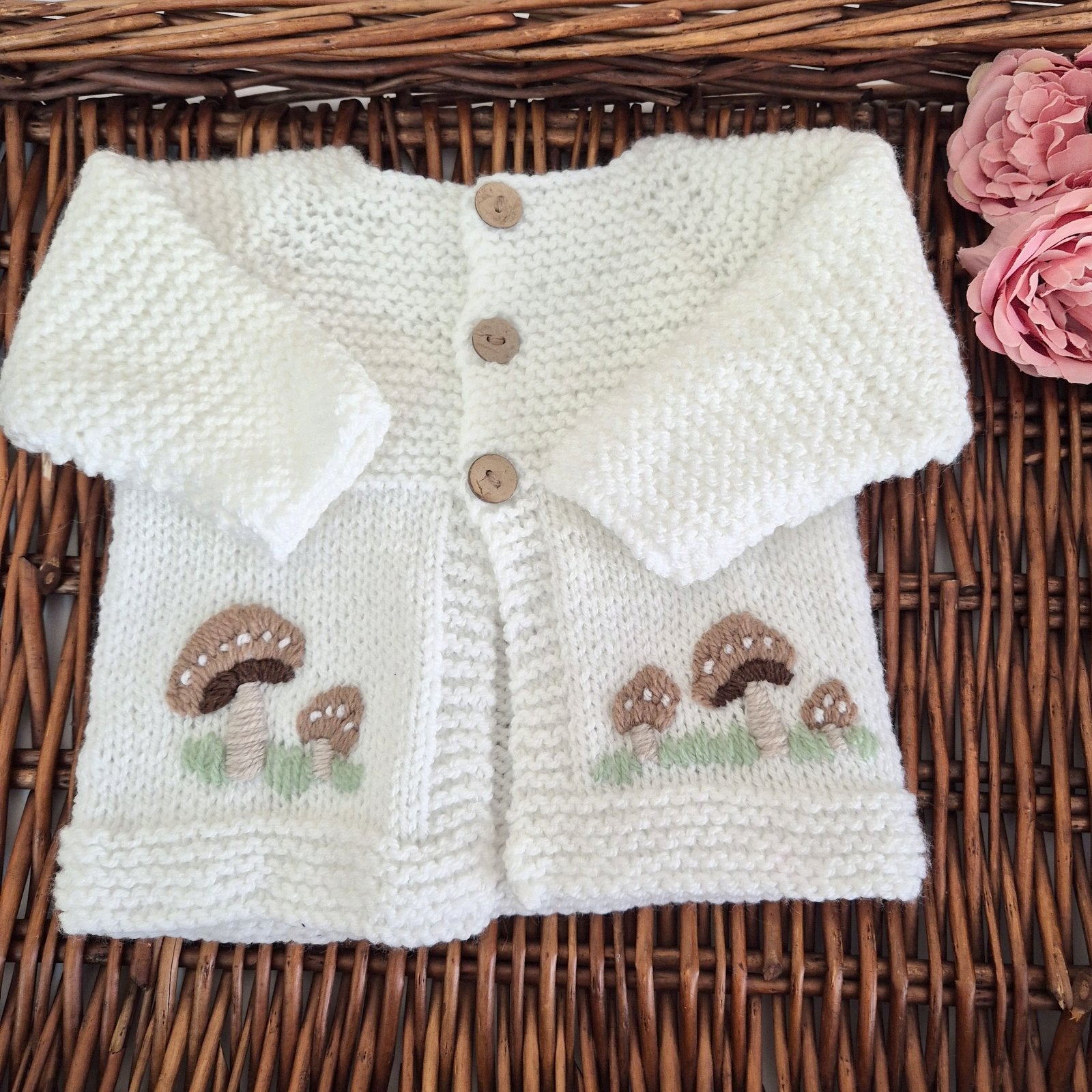 Knitted baby cardigan with mushroom patterns on a wicker surface