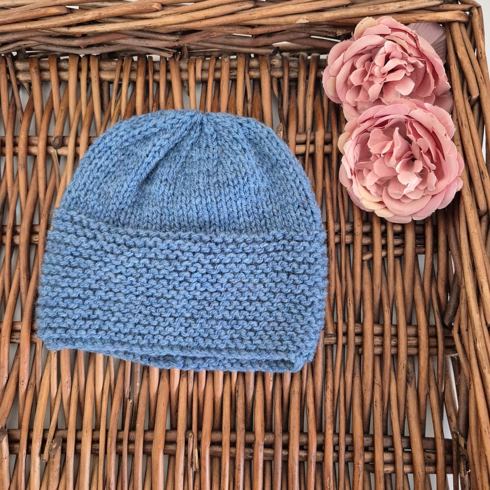 Blue knitted beanie on a woven surface with pink flowers
