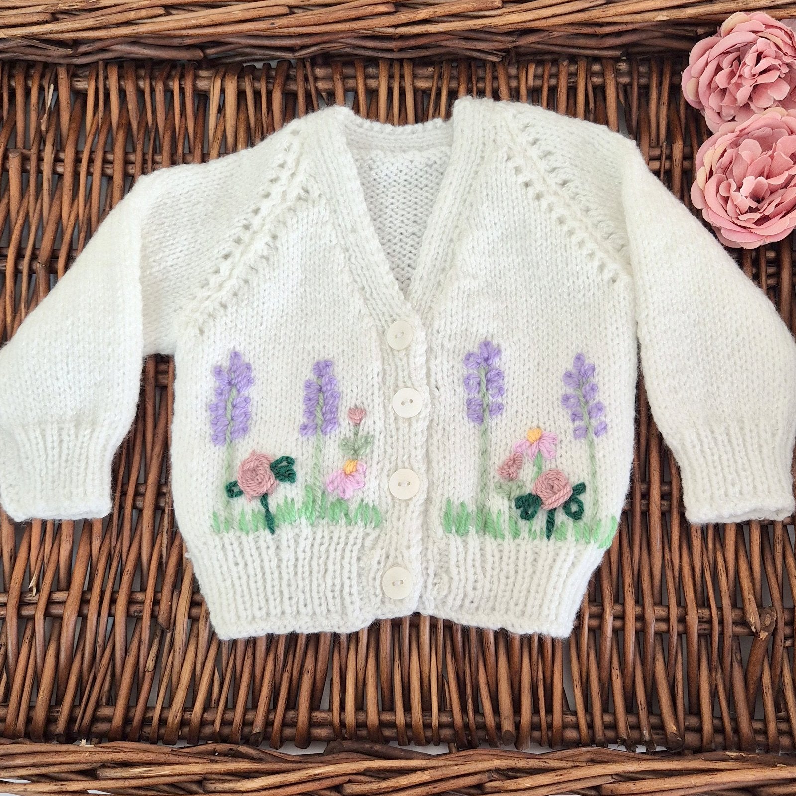 Ready to send handknit white baby cardigan for newborns aged 0–3 months. This charming cardigan features a classic v-neck, front button closure, and delicate embroidered roses, lavender, and flowers across the chest.

Perfect as a baby shower gift or part of a hospital coming home outfit, this one-of-a-kind piece arrives beautifully presented in an organza gift bag.