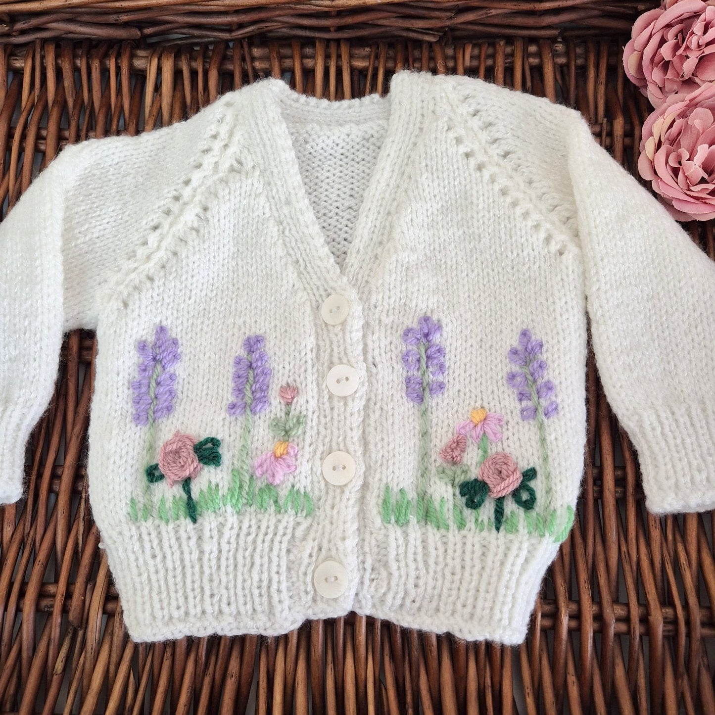Ready to send handknit white baby cardigan for newborns aged 0–3 months. This charming cardigan features a classic v-neck, front button closure, and delicate embroidered roses, lavender, and flowers across the chest.

Perfect as a baby shower gift or part of a hospital coming home outfit, this one-of-a-kind piece arrives beautifully presented in an organza gift bag.