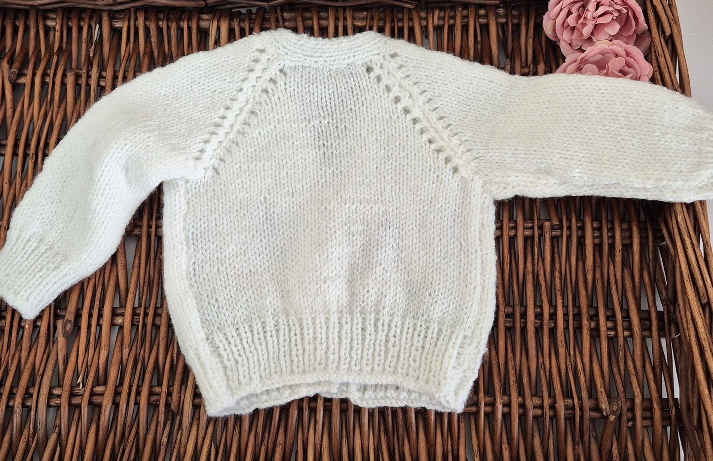 White knitted baby sweater on a wicker surface