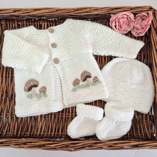 White hand knit baby cardigan, hat and booties set. Embroidered with little brown button mushrooms. Jumper, 0-6 months Sweater.

This cardigan has a raised pattern on the chest, with coconut shell buttons, and toadstool embroidery on the front. A matching white hat and booties complete the set.

Knit in soft acrylic yarn, easy for a busy mum to wash.
