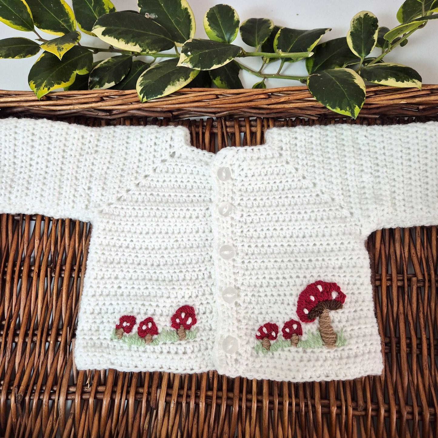 White crocheted cardigan with red mushroom designs on a woven surface