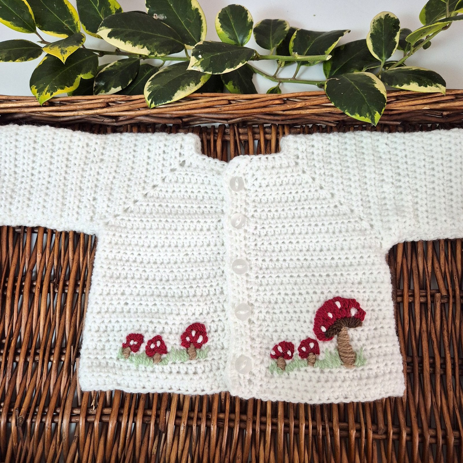 White crocheted cardigan with red mushroom designs on a woven surface