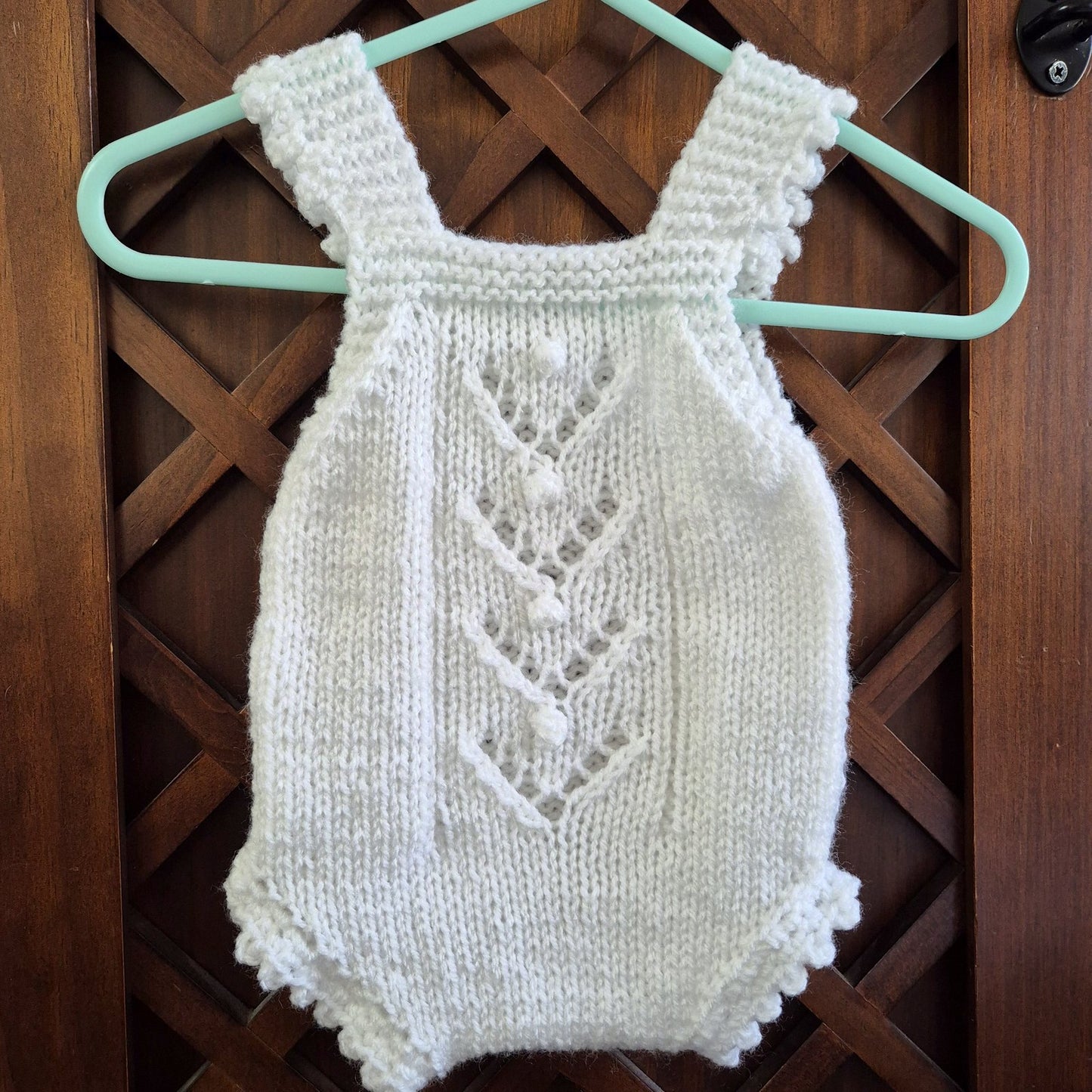 A sweet handknit lace and popcorn romper for a baby girl from newborn to 3 months old.

The darling little romper has a lace and popcorn pattern panel down the front, with scalloped frill on the legs and shoulder straps.