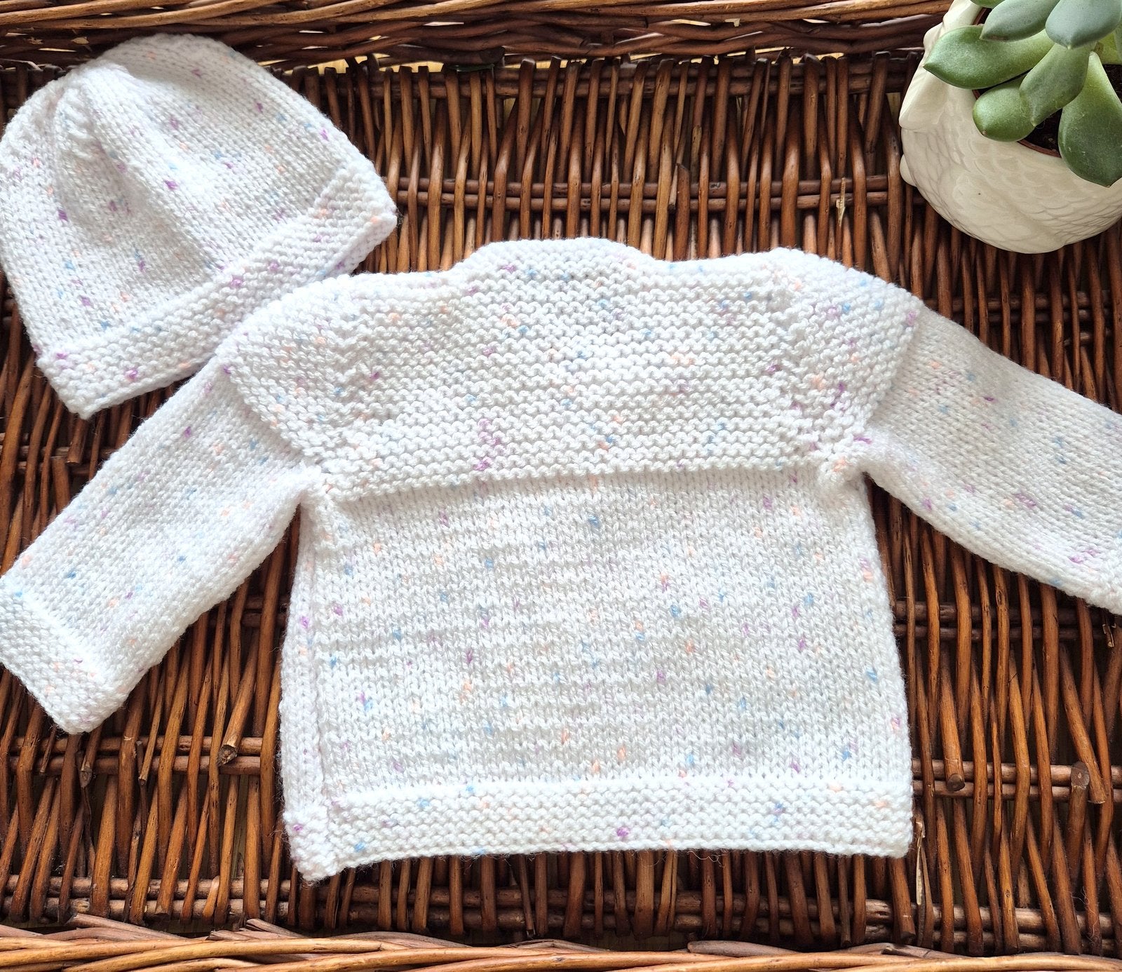 White knitted baby sweater and hat on a woven surface